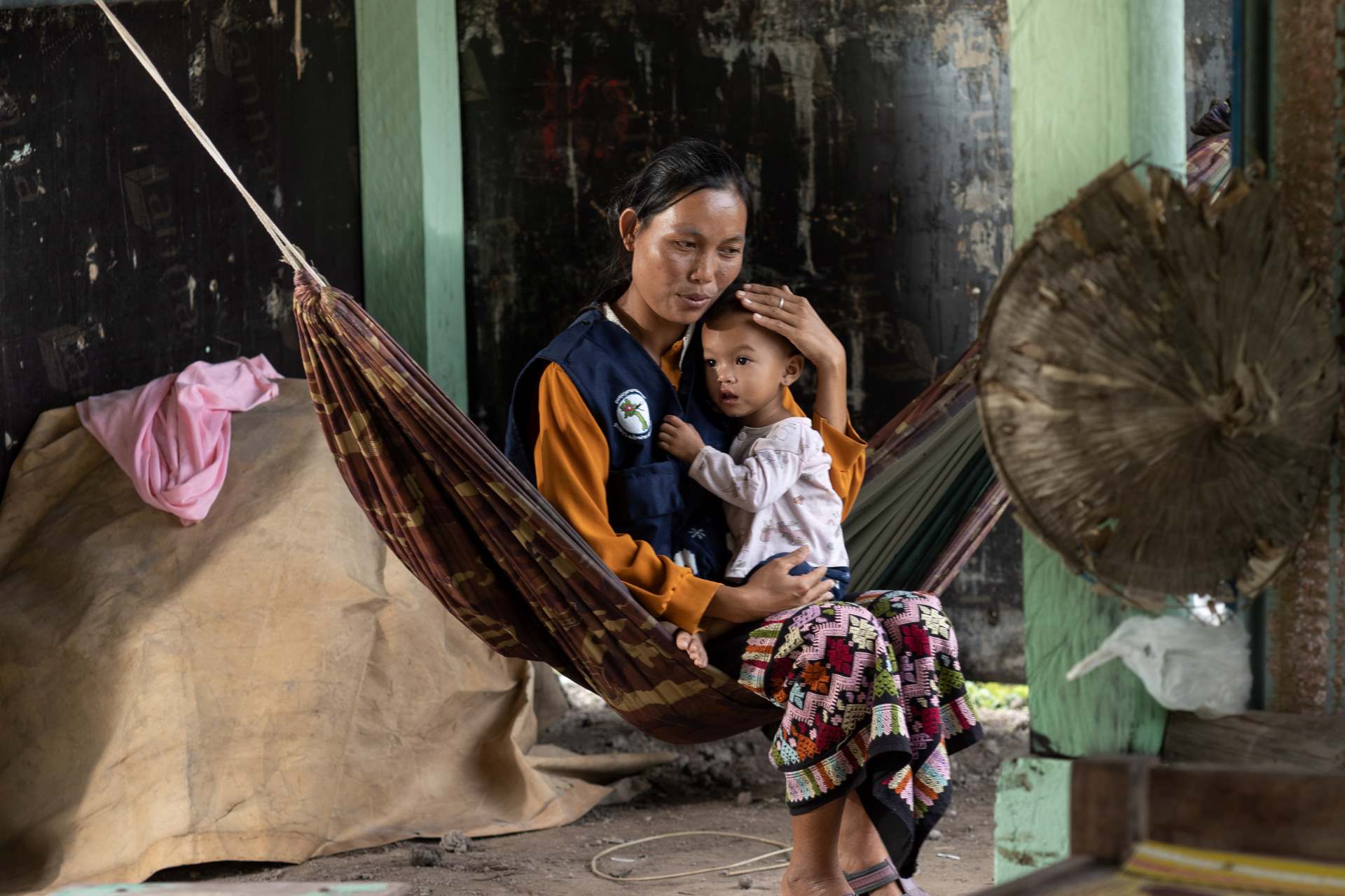 A WHO staff comforts a child while sitting in a hammock